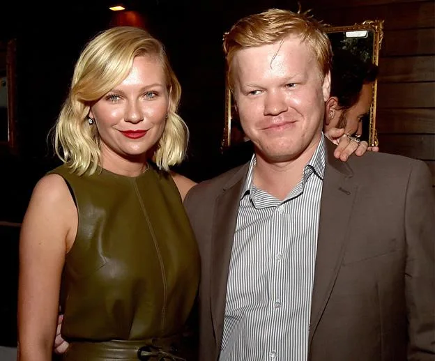 A woman in a green dress, smiling, with blond hair, standing next to a man in a suit at an event.