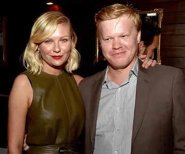 A woman in a green dress, smiling, with blond hair, standing next to a man in a suit at an event.