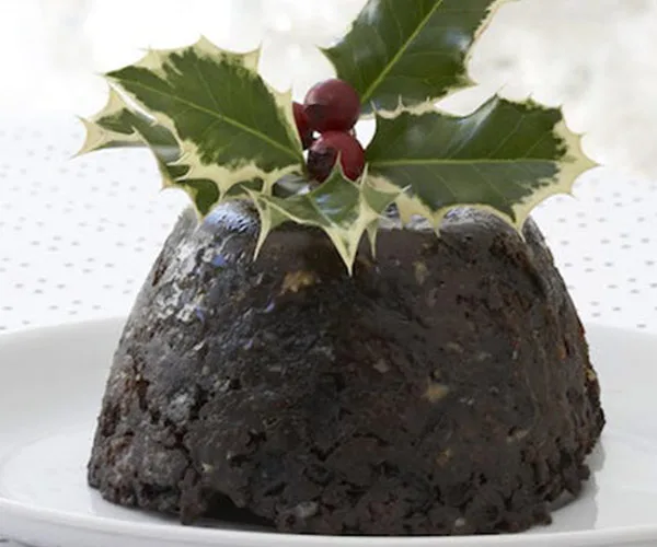 Christmas pudding topped with holly leaves and berries on a white plate.