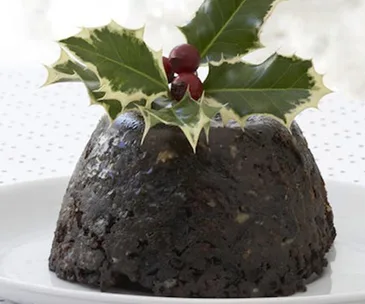 Christmas pudding topped with holly leaves and berries on a white plate.