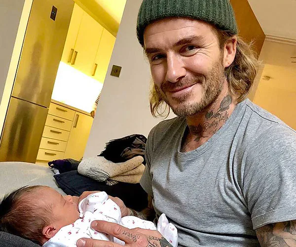 Man smiling while holding a newborn baby in a cozy home setting.