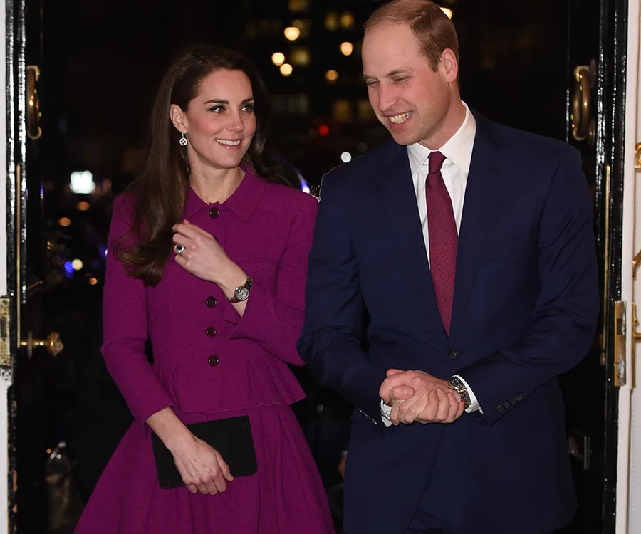 Prince William and Duchess Kate attending a formal event, she wears a purple dress, he wears a blue suit with red tie.