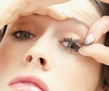 Close-up of a woman's face, pulling at her eyelashes, possibly to check for mites or dirt.