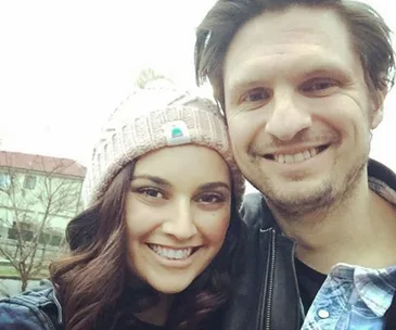 A smiling man and woman take a selfie outdoors; the woman is wearing a knit hat.