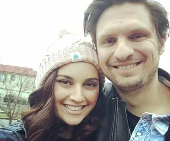 A smiling man and woman take a selfie outdoors; the woman is wearing a knit hat.