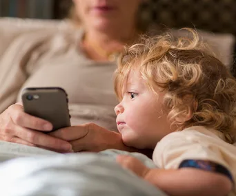 Parent and child relaxing while looking at a smartphone screen in bed.