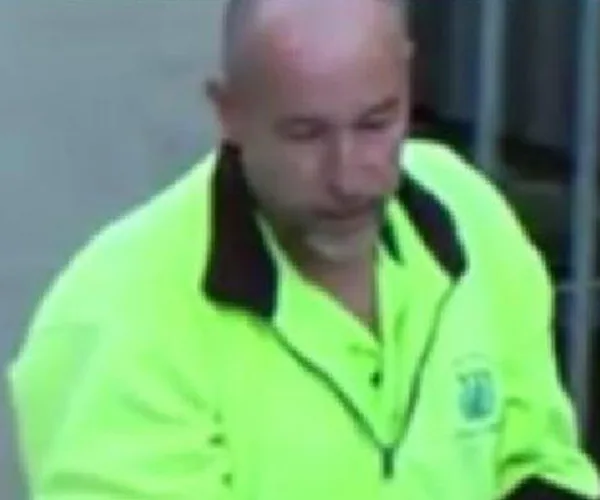 Man in high-visibility jacket, indoors, with blurred background.