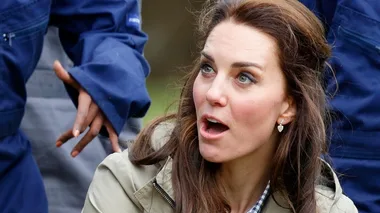 Kate Middleton looking surprised, wearing a jacket, with a person gesturing beside her, in an outdoor setting.