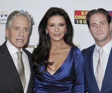 Three people posing on a red carpet, with one man in a suit and two others in elegant attire.