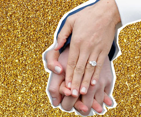 Hands with an oval engagement ring against a gold glitter background.