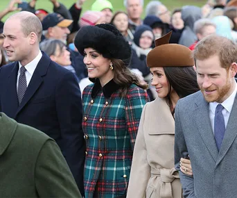 Four people walking together, dressed warmly in coats and hats, with a festive crowd in the background.