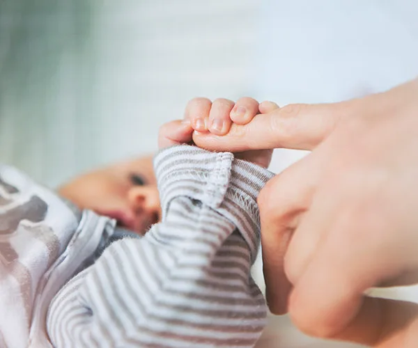 Baby in striped outfit holds adult's finger gently, symbolizing connection and care.