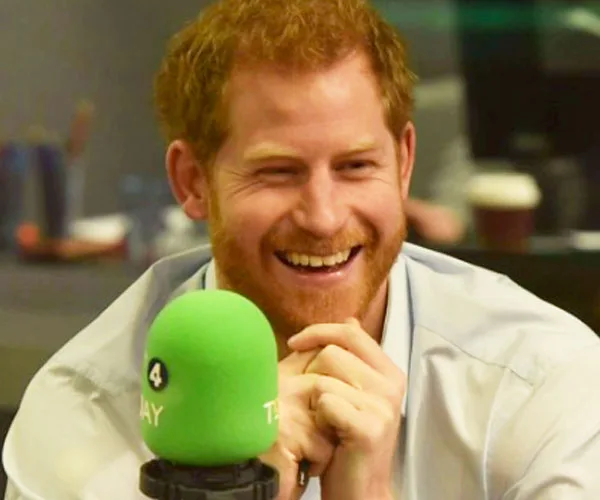 Prince Harry smiling behind a green microphone during a radio interview.