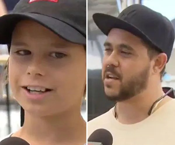 Two people side by side, both wearing black caps, speaking into microphones outdoors.