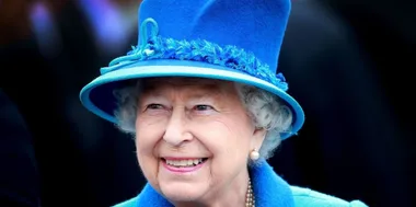 A woman in a bright blue hat and coat, smiling warmly.