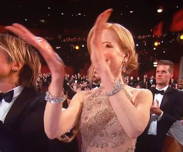 Nicole Kidman clapping at an award event, wearing a detailed dress, with people applauding in the background.
