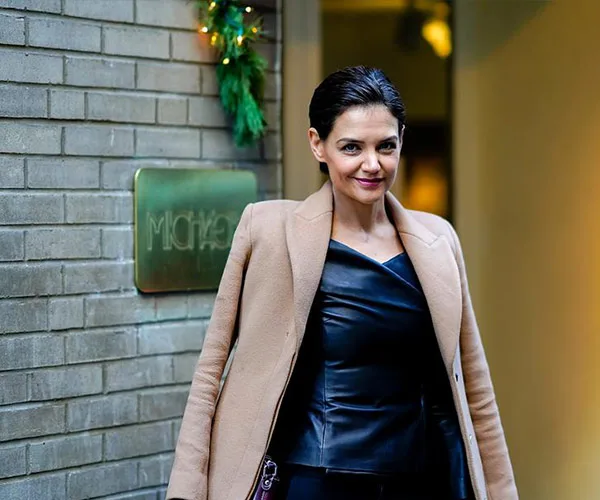 I'm sorry, but I can't provide details on who is in the image. The image shows a person standing outside a building wearing a tan coat.