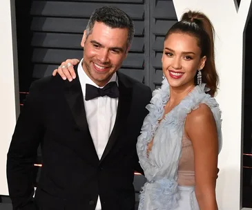 A man in a black suit and bow tie poses with a woman in a light blue dress at an event, both smiling.