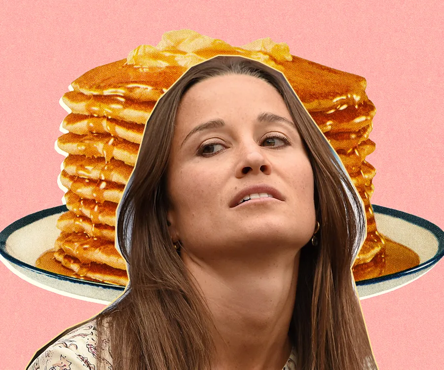 A woman looks up with a stack of pancakes with syrup in the background on a pink backdrop.