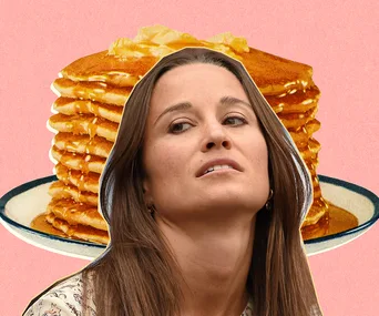 A woman looks up with a stack of pancakes with syrup in the background on a pink backdrop.