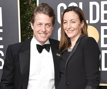 Man in a black tuxedo with a woman in a black outfit smiling at a formal event.