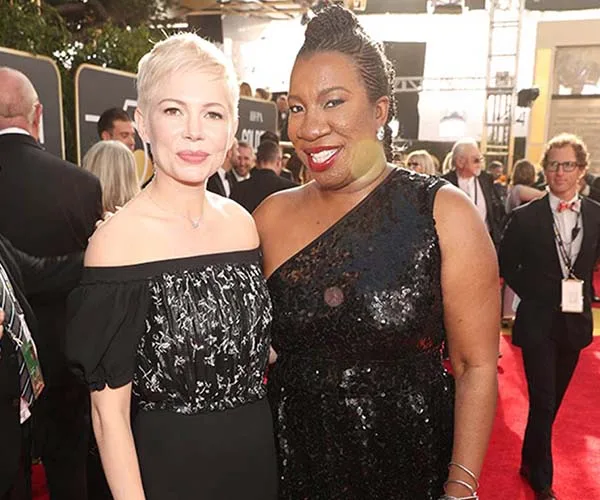 Two women smiling on the red carpet at a formal event, wearing elegant black dresses.
