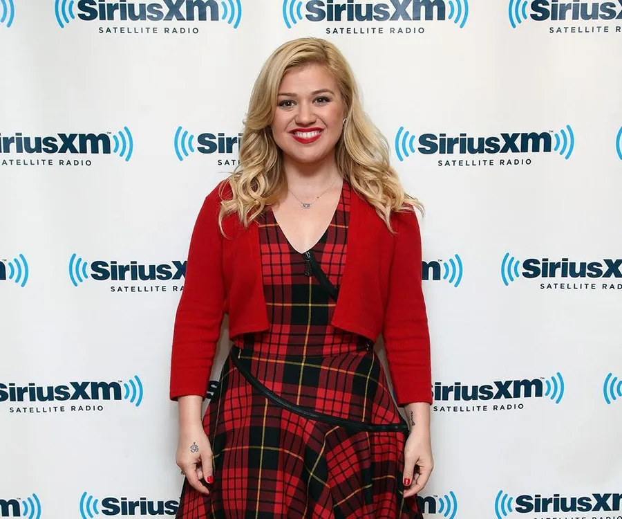 Singer in red plaid dress smiling in front of SiriusXM backdrop.