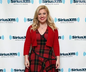 Singer in red plaid dress smiling in front of SiriusXM backdrop.