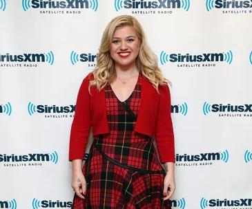 Singer in red plaid dress smiling in front of SiriusXM backdrop.