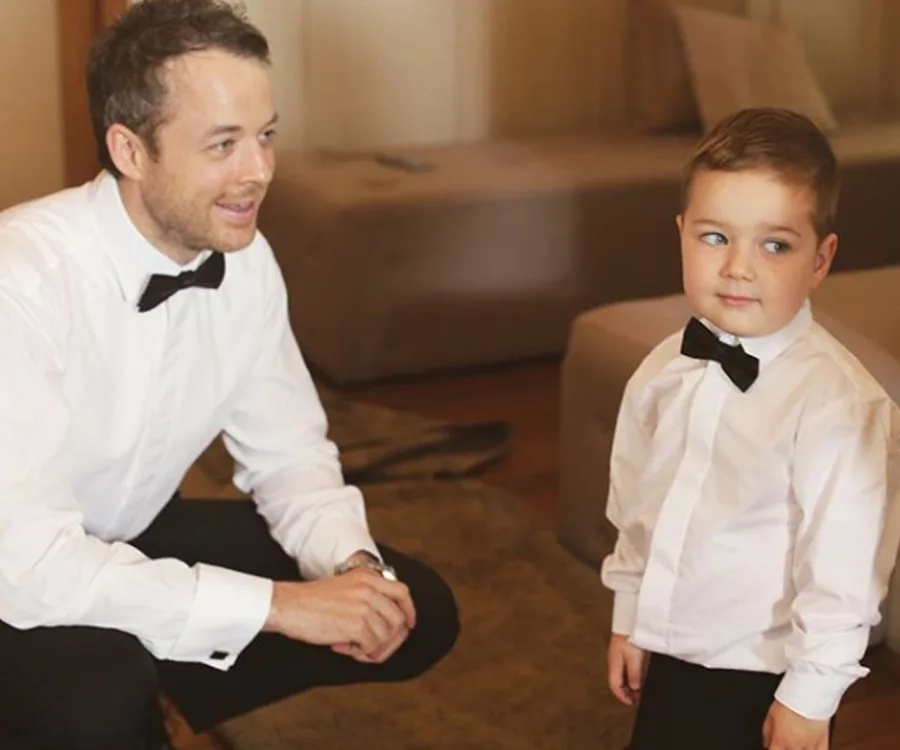 Man kneeling beside young boy; both in white shirts and black bow ties.