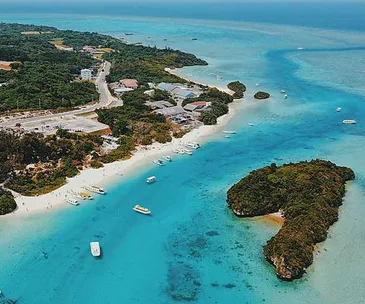 Aerial view of Ishigaki Island with turquoise waters, sandy beaches, and lush greenery, featuring boats along the coastline.