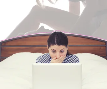 A surprised woman looks at a laptop screen on a bed with a blurred background image.