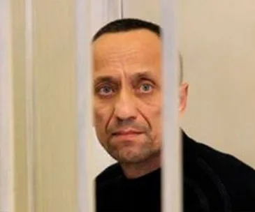 A man with short hair and a serious expression looks through vertical bars.