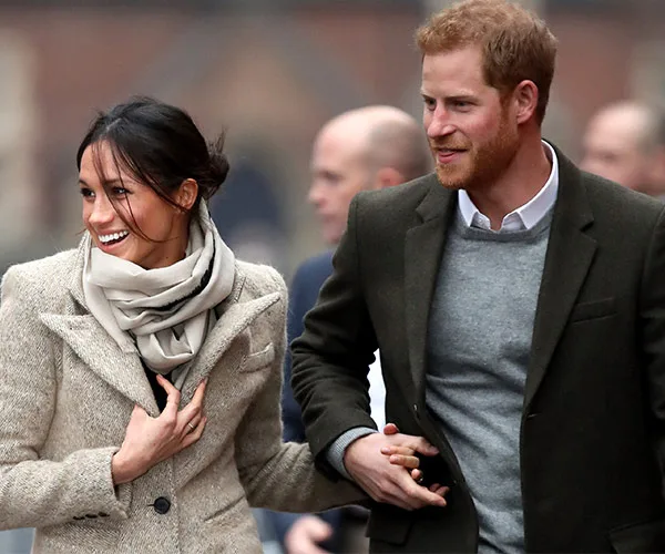 Couple walking and holding hands, smiling warmly at each other amidst a crowd in outdoor chilly weather.
