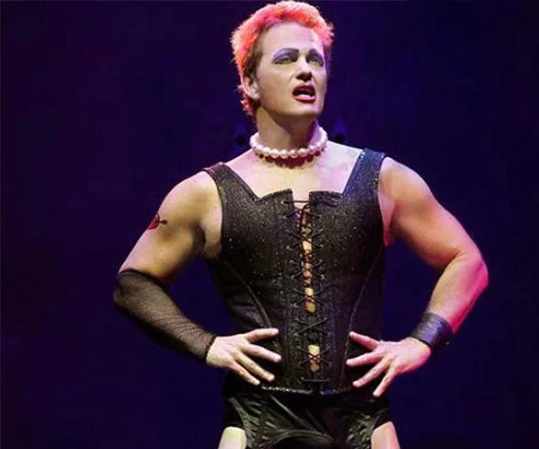A performer wearing a corset and pearl necklace on stage, in character with dramatic lighting.