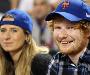 A couple wearing blue baseball caps, smiling and enjoying a sports event.