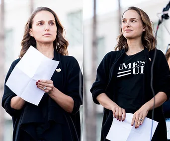Natalie Portman speaking at an outdoor event, holding a paper, wearing a "Time's Up" T-shirt and black cardigan.