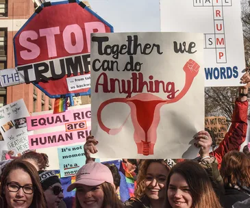 Protesters at Women's March holding signs, including uterus illustration with "Together we can do anything."