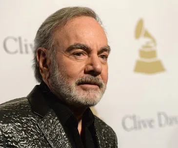 Man in a shimmering jacket poses at an event with Grammy and "Clive Davis" signage in the background.