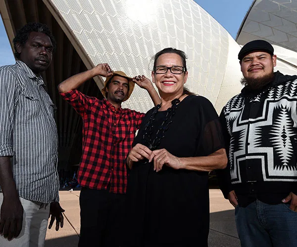 Group of four people standing in front of the Sydney Opera House, smiling and posing for the camera.