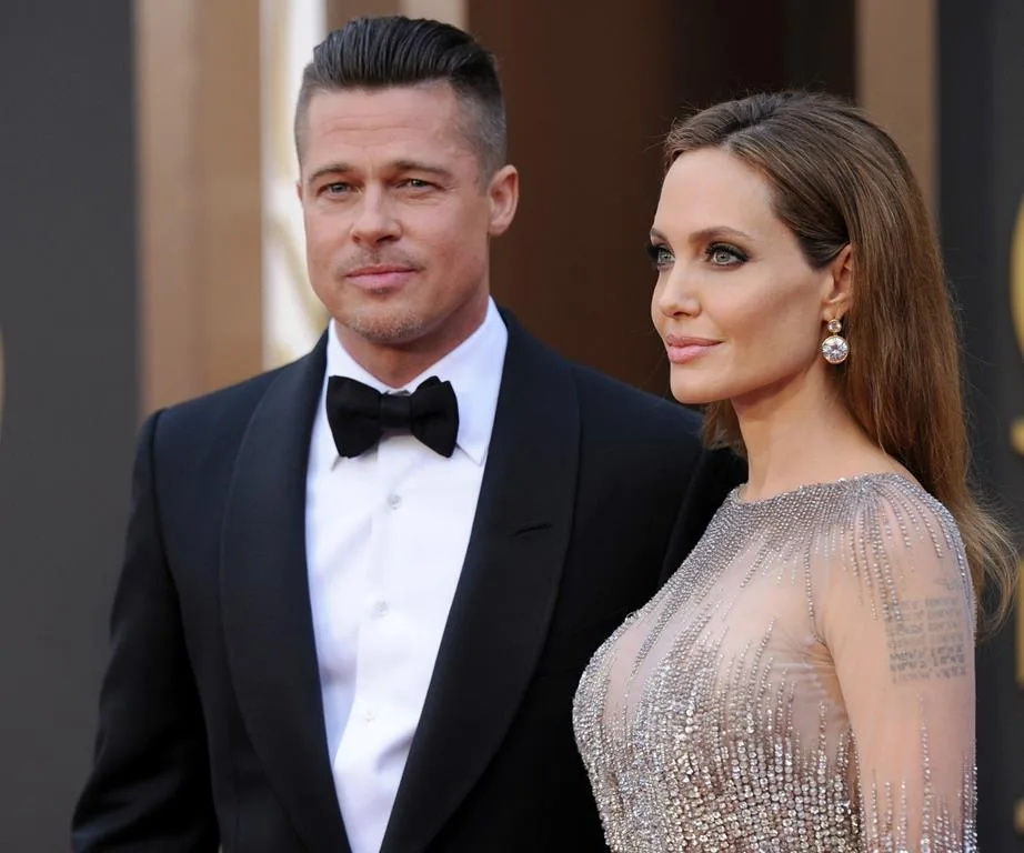 Two well-dressed individuals at a formal event, posing together; one in a tuxedo and the other in a shimmering gown.
