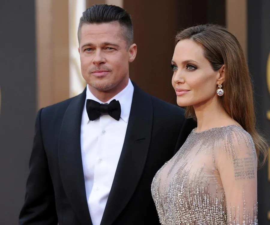 Two well-dressed individuals at a formal event, posing together; one in a tuxedo and the other in a shimmering gown.