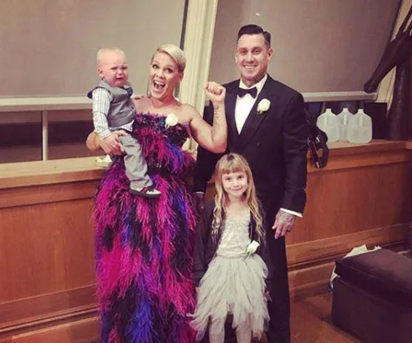 A family posing happily; woman in colorful dress holding a child, man in suit, and a girl in a light-colored dress.