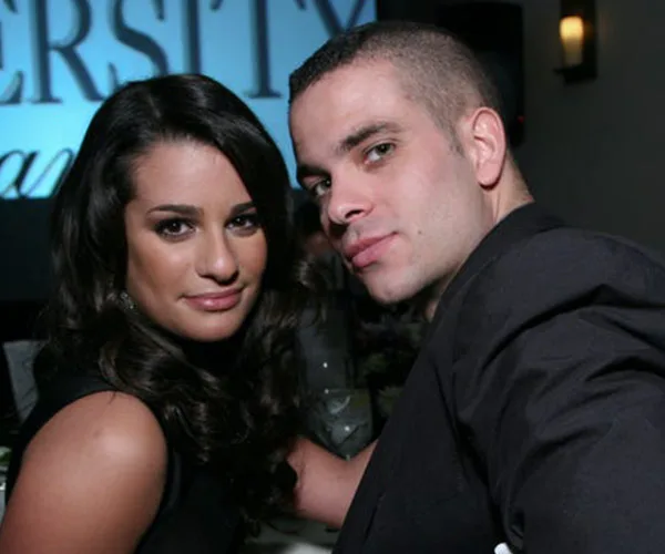Two individuals seated together, facing the camera, both wearing formal attire at an event.