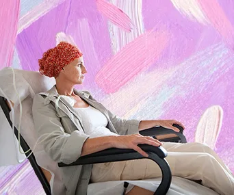 Woman wearing a red knitted beanie sitting in a chair against a pink abstract background.