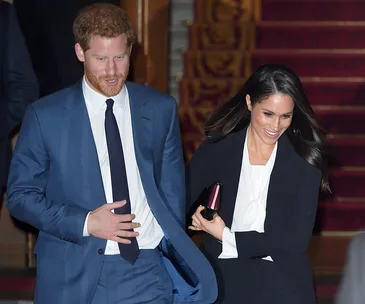 Prince Harry and Meghan Markle walking down a staircase, smiling at a military awards event.