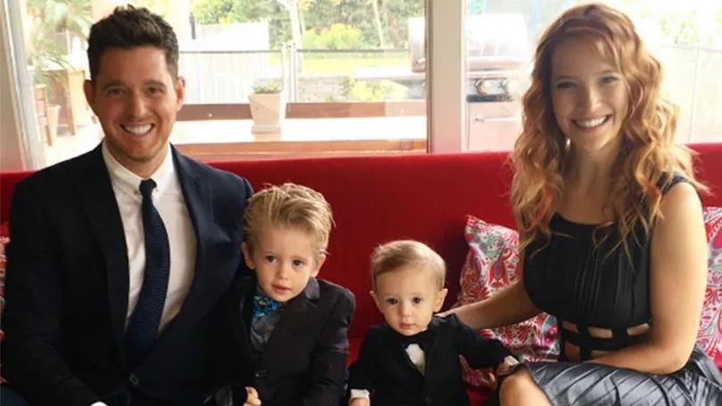 A family with two parents and two young children in suits sitting on a red sofa, smiling at the camera.