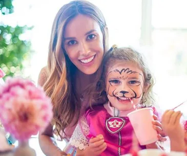 Mother and daughter smiling; daughter has animal face paint and pink cup.