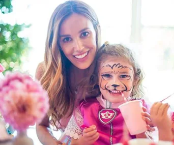 Mother and daughter smiling; daughter has animal face paint and pink cup.