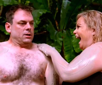 A couple laughing and applying mud on each other during a tropical outdoor activity surrounded by green foliage.